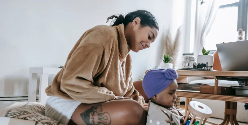 A mother beside her baby as the baby explores a wooden toy.