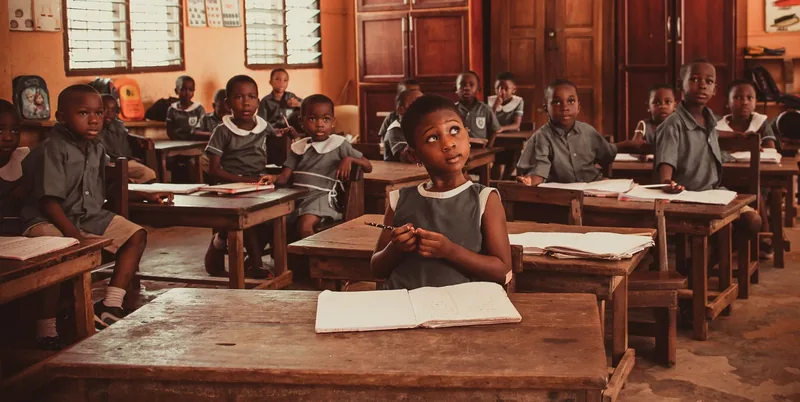 Primary school pupils seated at wooden desks with open exercise books.